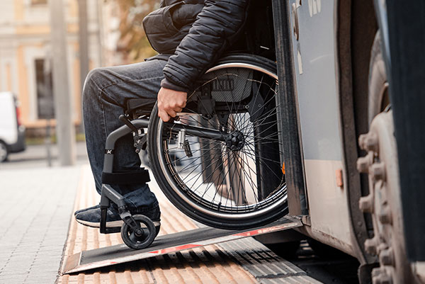 Rollstuhlfahrer fährt über eine Rampe aus dem Bus raus.